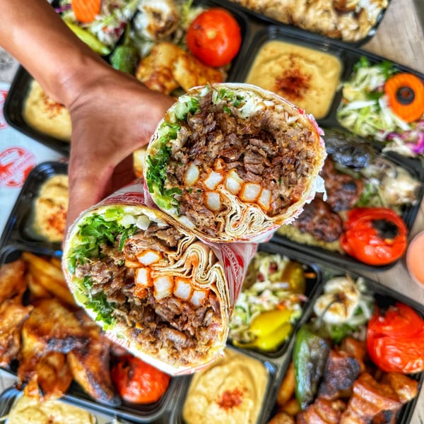 A hand holds a sliced Ara's Shawarma wrap filled with meat and fries, surrounded by various sides.