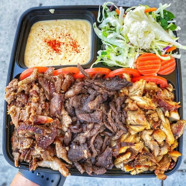 Ara's Shawarma platter with beef and chicken shawarma, hummus, salad, and sliced tomatoes.