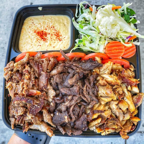 Ara's Shawarma platter with beef and chicken shawarma, hummus, salad, and sliced tomatoes.