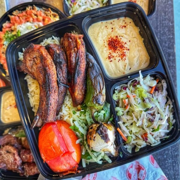 Ara's Shawarma takeout container with grilled chicken, rice, hummus, salad, and roasted vegetables.