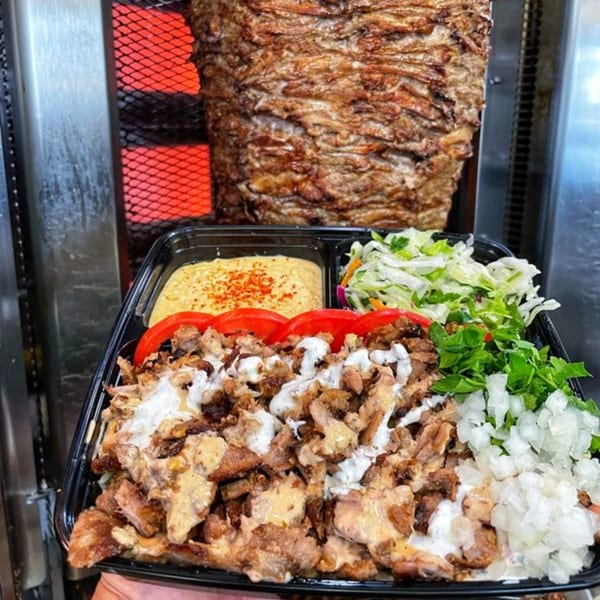 Ara's Shawarma plate with meat, hummus, salad, and onions, next to a large shawarma spit.
