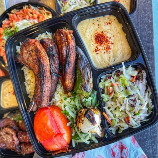 Ara's Shawarma takeout container with grilled chicken, rice, hummus, salad, and roasted vegetables.