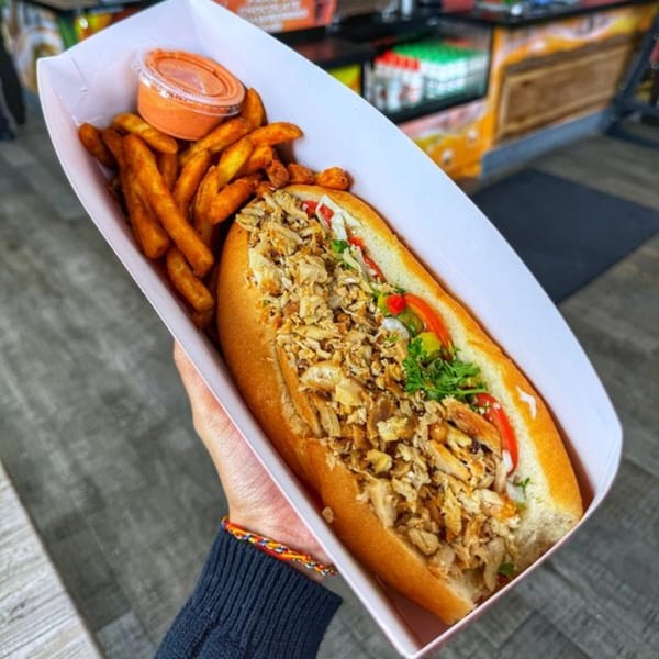 Hand holding a tray with a chicken shawarma sub, fries, and dipping sauce.